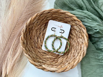 Pair of green and beige hoop earrings on a card with a wicker basket and green fabric in the background.